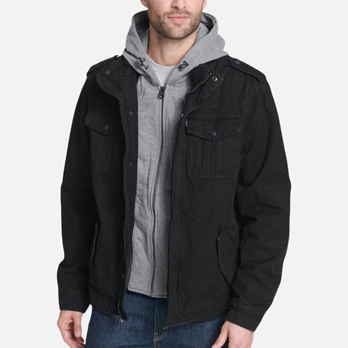 A man wearing a black hooded jacket over a gray hoodie and blue jeans.