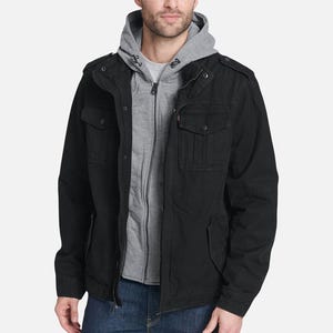 A man wearing a black hooded jacket over a gray hoodie and blue jeans.