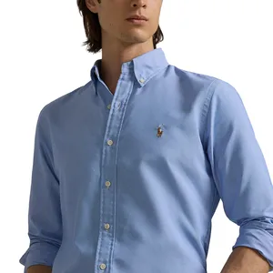 A person is wearing a light blue button-up shirt with rolled-up sleeves, featuring a small embroidered polo logo on the chest.