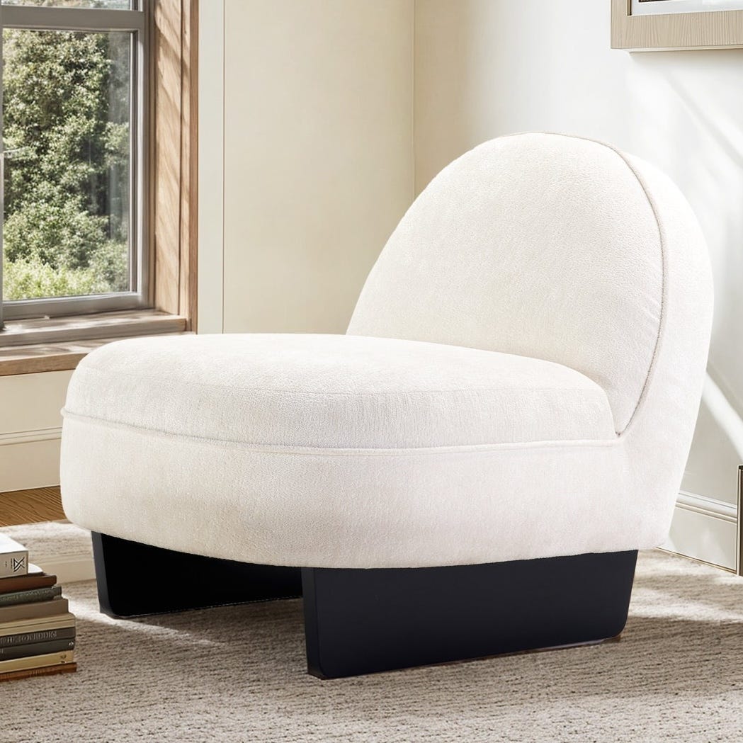 A modern armless white accent chair with a rounded back and thick cushioned seat, featuring a dark, sturdy base, placed on a textured rug near a window.