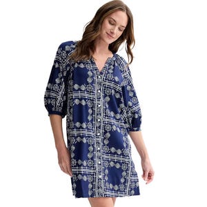 A woman is wearing a navy blue dress with white geometric patterns, featuring a V-neckline and three-quarter sleeves.
