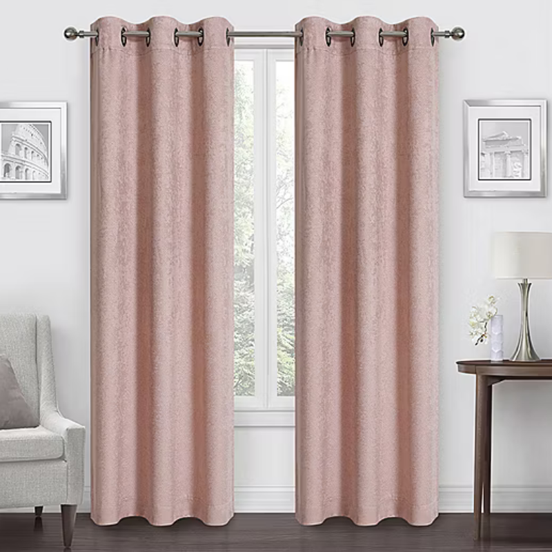 Room with pink curtains on a metal rod, flanked by two framed pictures. A lamp and flowers rest on a side table, with an armchair on the opposite side.