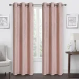 Room with pink curtains on a metal rod, flanked by two framed pictures. A lamp and flowers rest on a side table, with an armchair on the opposite side.