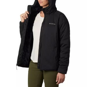 A black Columbia hooded jacket with white lining and branding on the chest, paired with green pants.