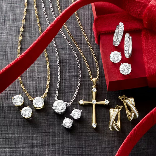 A collection of gold and silver jewelry featuring necklaces with pendants, including a cross, stud earrings with round stones, and hoop earrings, displayed with a red velvet ribbon and gift box.