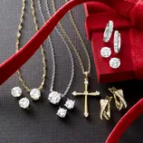 A collection of gold and silver jewelry featuring necklaces with pendants, including a cross, stud earrings with round stones, and hoop earrings, displayed with a red velvet ribbon and gift box.