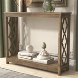 A wooden console table with decorative lattice side panels, featuring several books and decorative objects like a white textured sphere and ornate finial.