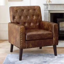 A brown leather armchair with a tufted backrest and nailhead trim, featuring wooden legs, set in a living room with a fireplace in the background.