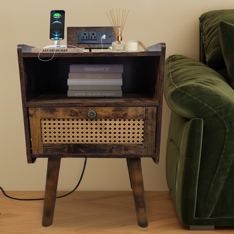 A wooden bedside table with rattan drawer features a charging phone, aromatherapy diffuser, a candle, and stacked books, positioned beside a green sofa.