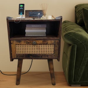 A wooden bedside table with rattan drawer features a charging phone, aromatherapy diffuser, a candle, and stacked books, positioned beside a green sofa.