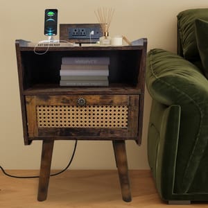 A wooden bedside table with rattan drawer features a charging phone, aromatherapy diffuser, a candle, and stacked books, positioned beside a green sofa.