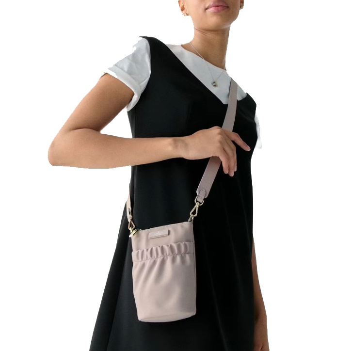 A person wearing a black dress layered over a white shirt holds a small, light pink crossbody bag with a ruffled design.