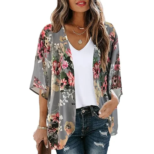 A woman wearing a white V-neck t-shirt and a floral print kimono with varying shades of pink, green, and grey flowers. She also has on ripped blue jeans.