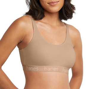 A woman is wearing a tan Hanes sports bra with a scoop neckline and branded elastic band.