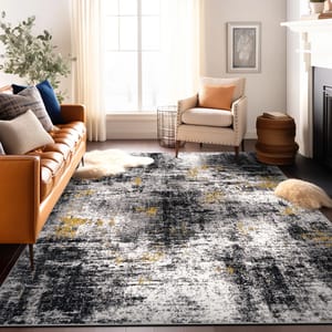 A modern area rug in black, gray, and white with gold accents, featuring an abstract brushstroke pattern, lies on a wooden floor beside a tan leather sofa and cream-colored armchair.
