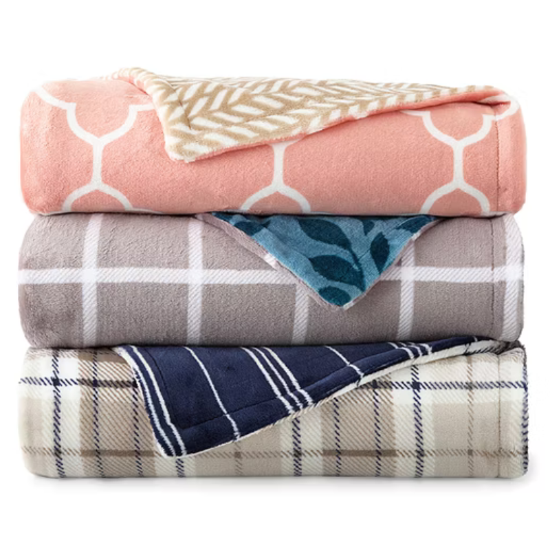 Three stacked blankets with different patterns: pink with white hexagons, gray with white squares, and blue with plaid. Each blanket shows a contrasting pattern on the fold.