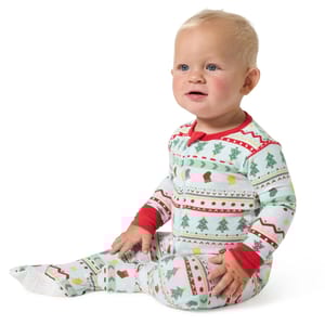 A baby is wearing snug-fitting pajamas with a Fair Isle pattern featuring holiday motifs in red, green, and white colors.