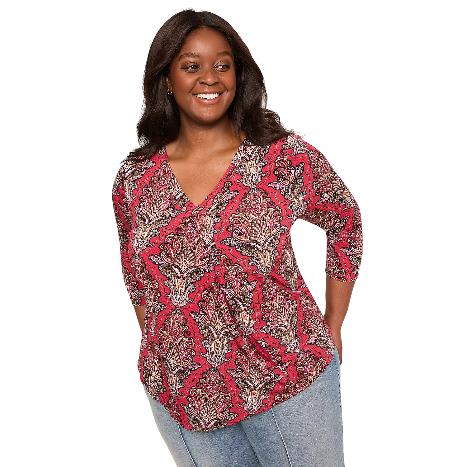A woman is wearing a red paisley-patterned V-neck top with 3/4 sleeves and light blue jeans, smiling with hands on hips.