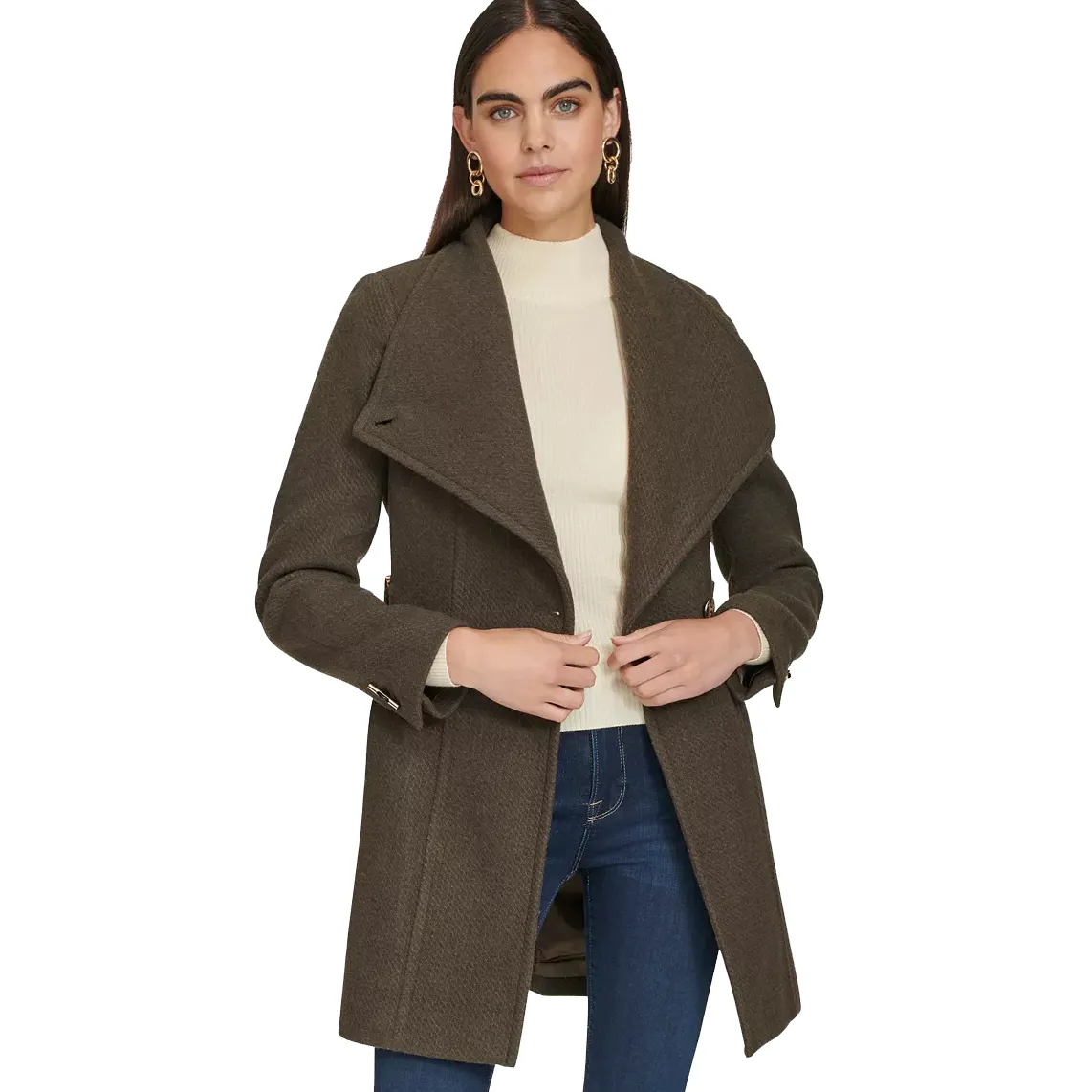 A woman is wearing a brown coat with a wide collar over a white turtleneck sweater, paired with blue jeans and gold earrings.