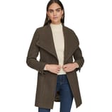 A woman is wearing a brown coat with a wide collar over a white turtleneck sweater, paired with blue jeans and gold earrings.