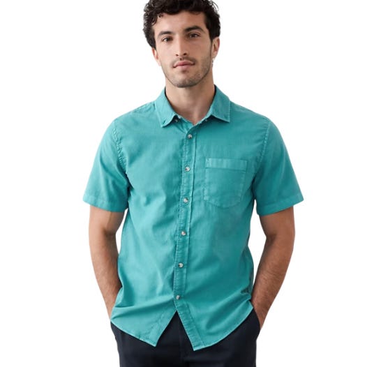 A man wears a short-sleeve, teal button-up shirt with a front pocket, paired with dark pants.