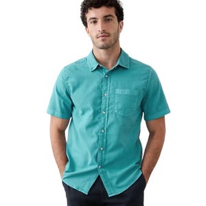 A man wears a short-sleeve, teal button-up shirt with a front pocket, paired with dark pants.