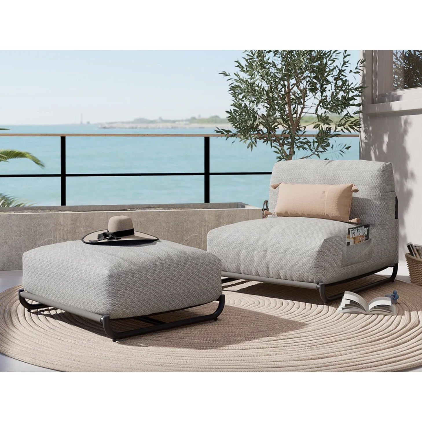 Outdoor lounge chair with matching ottoman, both in light gray fabric, on a circular beige rug, with coastal backdrop.