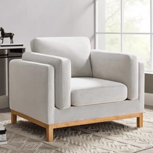A modern armchair with a light grey fabric and wooden legs sits on a textured cream rug, near a window.