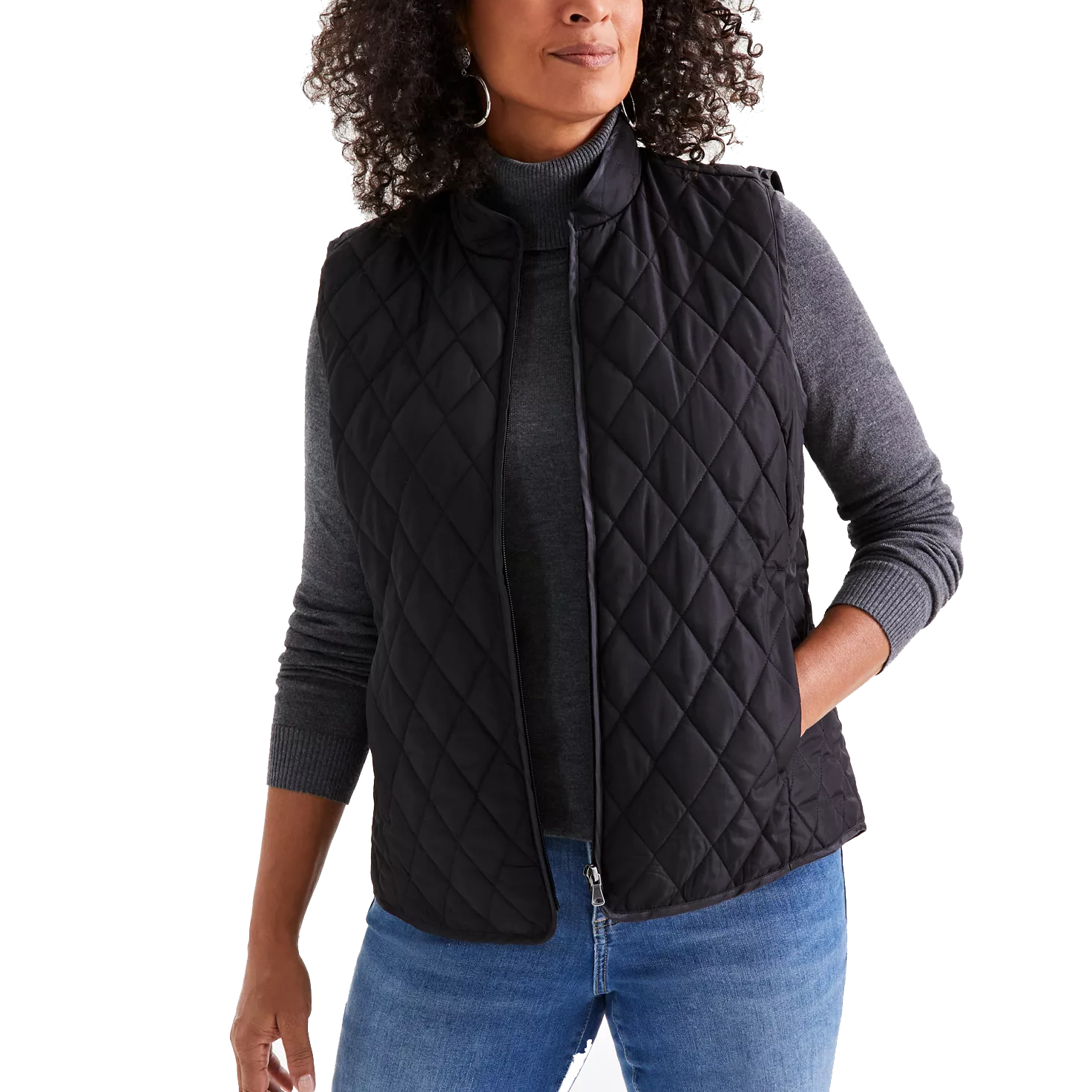 A woman is wearing a black quilted vest over a gray turtleneck sweater paired with blue jeans.