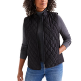 A woman is wearing a black quilted vest over a gray turtleneck sweater paired with blue jeans.