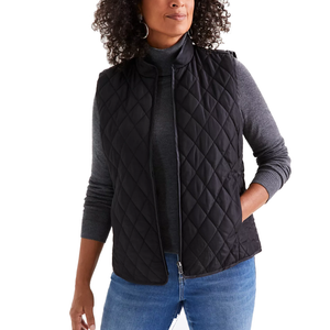 A woman is wearing a black quilted vest over a gray turtleneck sweater paired with blue jeans.