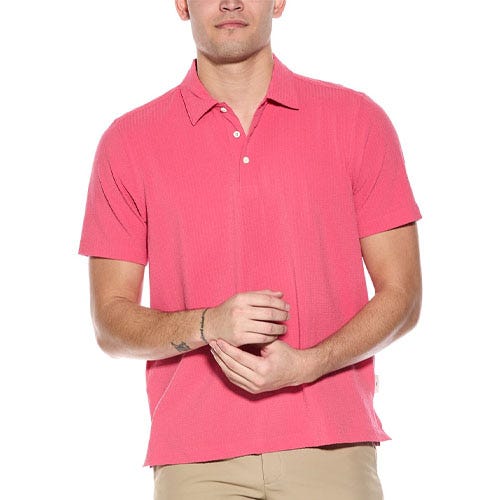 A pink short-sleeve Tommy Bahama polo shirt with a ribbed texture, featuring a classic collar and a three-button placket, paired with beige pants.