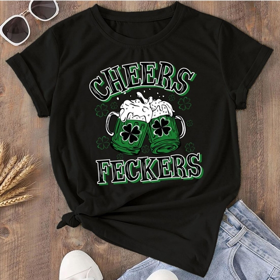 Black t-shirt featuring two green beer mugs with shamrocks, frothy beer spilling over, and the text \“CHEERS FECKERS\“ in bold, festive green and white lettering.
