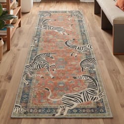 A runner rug with an ornate design in orange and blue features playful zebra motifs on a wooden floor beside a bench and plants.