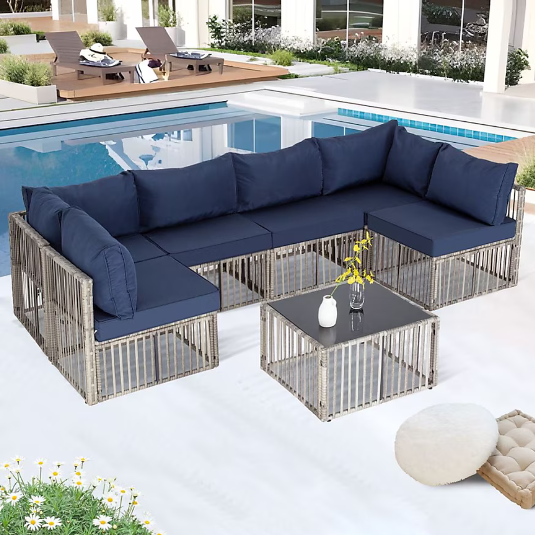 Outdoor sectional set with navy cushions and a matching coffee table near a poolside. The seating features a modern, open-frame design with light-colored frames and a glass-top table.