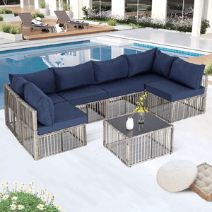 Outdoor sectional set with navy cushions and a matching coffee table near a poolside. The seating features a modern, open-frame design with light-colored frames and a glass-top table.