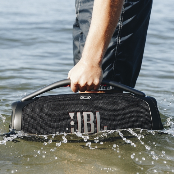 A person is holding a JBL portable speaker partially submerged in water.