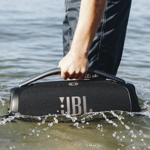 A person is holding a JBL portable speaker partially submerged in water.