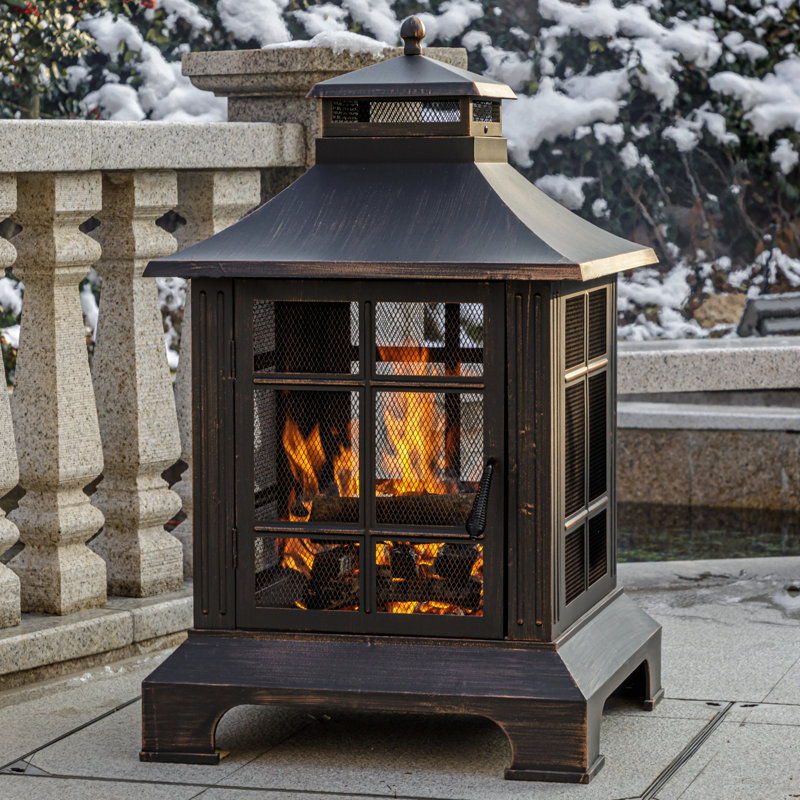 An outdoor metal fireplace with a mesh screen, a peaked roof, and a fire burning inside.