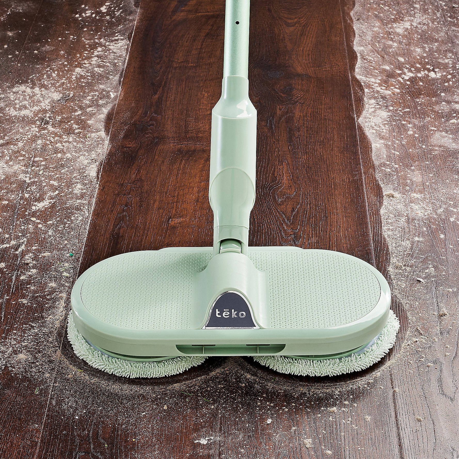 A mint green electric floor mop cleaning a wooden floor, half with scattered white powder, and half clean.