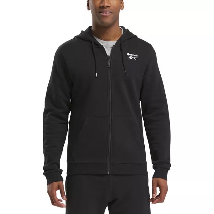 A person is wearing a black Reebok full-zip hoodie with a hood and front pockets, featuring a logo on the chest.