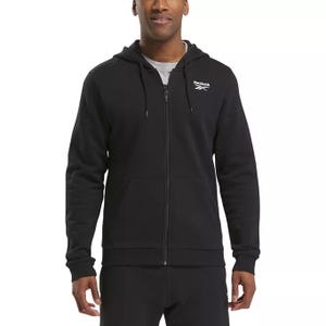 A person is wearing a black Reebok full-zip hoodie with a hood and front pockets, featuring a logo on the chest.