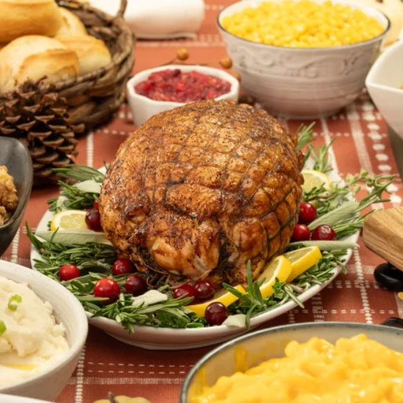 Roasted turkey surrounded by garnishes, with side dishes of corn, mashed potatoes, cranberry sauce, and biscuits in the background.