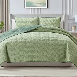 A light green quilted bedspread with a leaf pattern is displayed on a neatly made bed, accompanied by matching pillow shams. The bedding features a darker green trim and complements the light, neutral decor of the room.