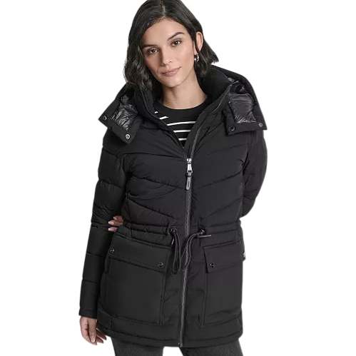 A woman wearing a stylish black puffer jacket with a hood and drawstring waist, paired with a black and white striped top and dark pants.