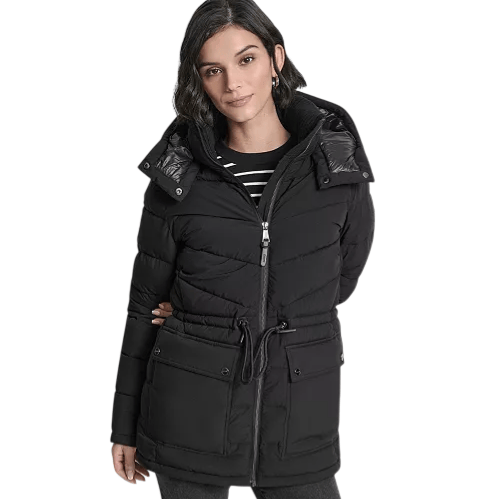 A woman wearing a stylish black puffer jacket with a hood and drawstring waist, paired with a black and white striped top and dark pants.