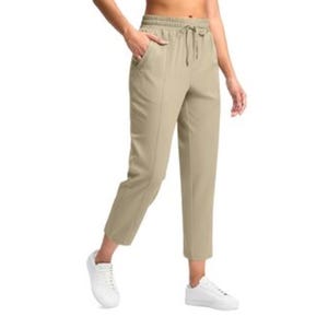 Woman wearing cropped, beige drawstring pants with pockets and white sneakers, modeling in a casual pose.