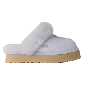 A light gray slip-on slipper with a fluffy fur trim, featuring a tan platform sole and the UGG logo on the side.