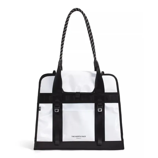 White and black tote bag with long textured handles, featuring The North Face logo and buckled front strap detailing.