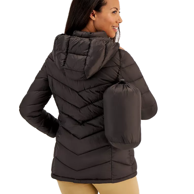 A woman wearing a dark, hooded quilted jacket is shown holding a matching drawstring stuff sack.